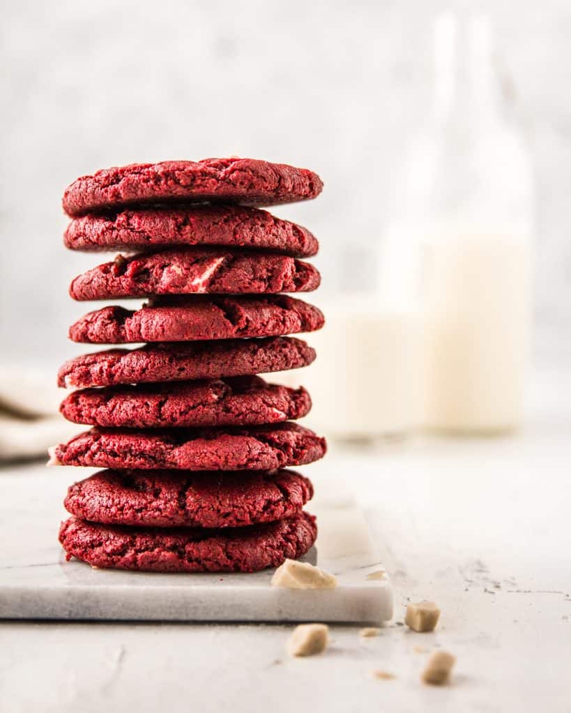 A stack of Vegan Red Velvet Cookies with white vegan white chocolate chunks and plant milk.