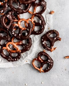 A pile of vegan chocolate and caramel dipped pretzels on parchment paper.