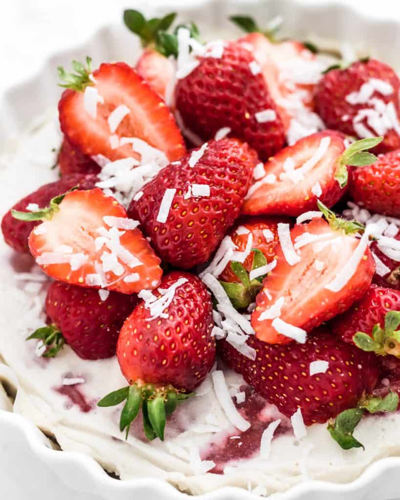 Vegan strawberry coconut ice cream cake with fresh strawberries and coconut shreds on top.