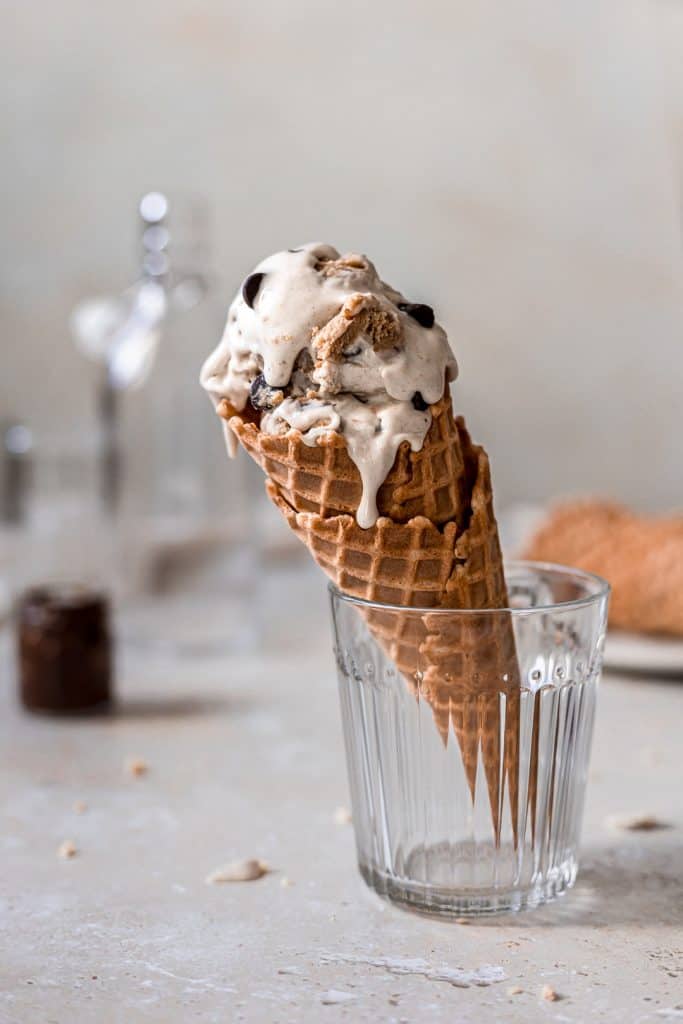 Melty chocolate chip cookie dough ice cream in a waffle cone, standing upright in a glass. 